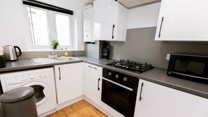 A modern kitchen with white cabinets, a stainless steel sink, a built-in oven, and a microwave. - Studio With Parking, By Uni/Hosp (Exeter)