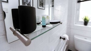 A bathroom with a glass shelf holding toiletries, a toilet, and a window with a plant. - Studio With Parking, By Uni/Hosp (Exeter)