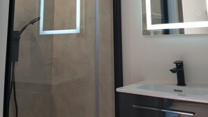 Een moderne badkamer met een douchecabine van glas, een witte wastafel met zwarte kraan en een spiegel met ingebouwde verlichting.