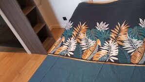 Een bed met een donkerblauwe spreideken met tropische bladmotieven, een houten hoofdbord en een houten vloer.