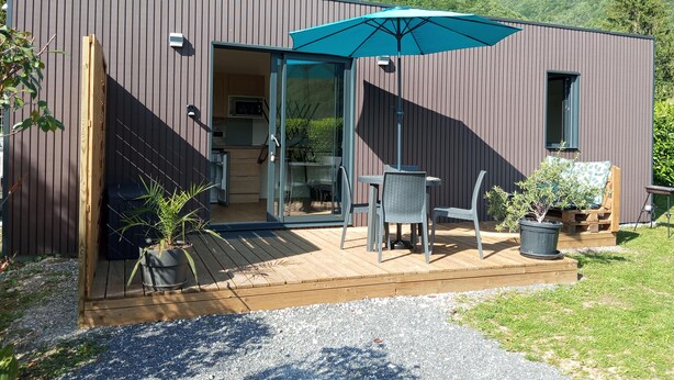 Een modern gebouw met een houten terras, een eethoek met tuinmeubilair en uitzicht op groene bergen.