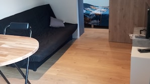 Een moderne leefruimte met een houten eettafel, een zwarte bank en een bed met een bladprint.