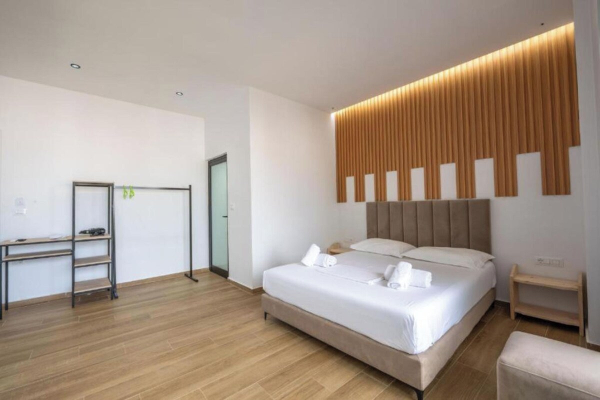 A modern hotel room with a large bed, a desk, and a wardrobe.