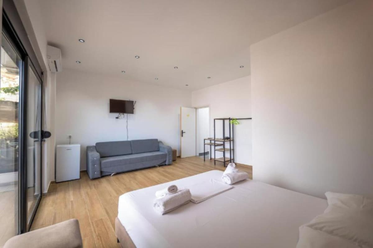 A modern hotel room with a bed, a sofa, a TV, and a small table.