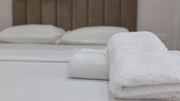 A neatly made bed with white linens and pillows, a wooden headboard, and a white wall with a wooden panel design. - Mece Apt (Sarandë)