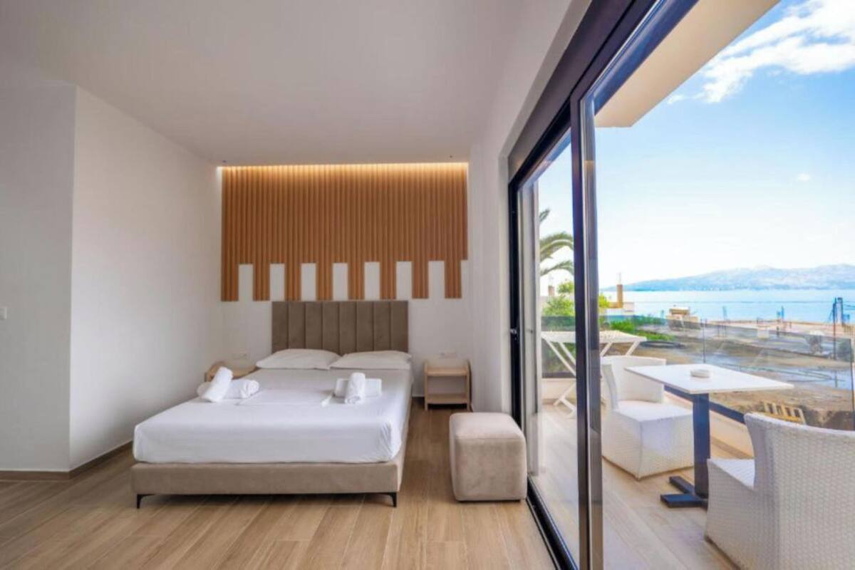 Quarto de hotel moderno com uma cama grande, mesa de cabeceira, área de estar pequena e varanda com vista para o mar.