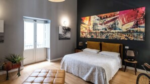 Une chambre avec un grand lit, un luminaire suspendu moderne, un grand tableau abstrait et une vue sur l’extérieur par une porte.