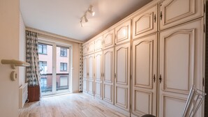 Ein geräumiges Zimmer mit großem Kleiderschrank, einem Sessel und Blick auf ein Gebäude durch ein Fenster.