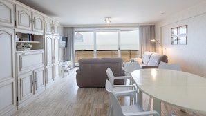 Ein modernes Hotelzimmer mit Balkon, einer Couch, einem Esstisch und einem Fernseher.