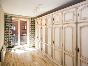 A spacious room with a large wardrobe, a chair, and a view of a red brick building through a glass door. - Charming Apartment With sea View (Middelkerke)
