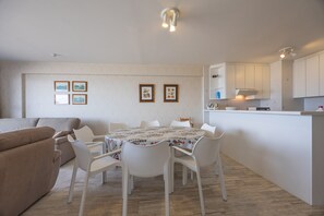 A modern living room with a dining area, white furniture, and a kitchen with white cabinets. - Charming Apartment With sea View (Middelkerke)