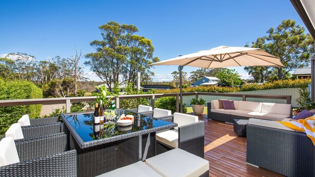 Un patio exterior con mobiliario de mimbre, una mesa con cubierta de vidrio y un paraguas grande.