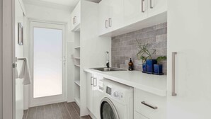 Una cocina moderna con armarios blancos, lavadora integrada, un lavabo y un salpicadero de azulejos.