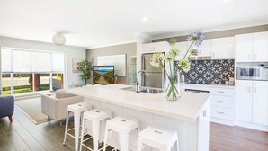 Una cocina moderna con armarios blancos, una isla grande con taburetes y un horno empotrado, con vistas al exterior.