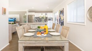 Un comedor con mesa de vidrio, sillas de madera y una mesa lista para el desayuno, con croissants, mermelada y jugo de naranja.