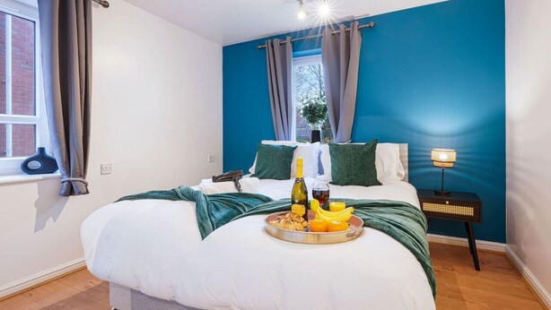 Ein Schlafzimmer mit Bett, Nachttisch mit Lampe, Fenster mit Vorhängen und einem Tablett mit Frühstücksangeboten.