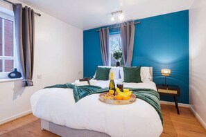 Quarto com cama, mesa de cabeceira com abajur, janela com cortinas e bandeja com itens de café da manhã.