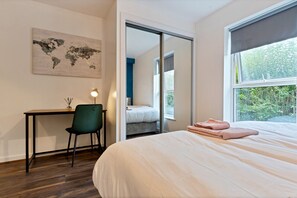Een slaapkamer met een bed, een bureau, een stoel, een wereldkaart als kunstwerk, en uitzicht op groen buiten.