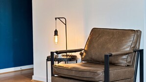 A brown leather chair with a metal frame and a side table, positioned against a white wall with a blue accent. - Stylish Apartment in City Centre with Free Parking (Chelmsford)
