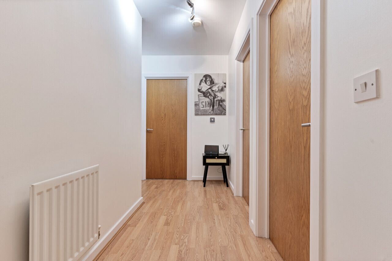 A hallway with wooden flooring, white walls, and a black side table with a laptop.