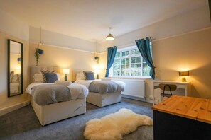 Ein Schlafzimmer mit zwei Betten, einem Schreibtisch, einem Stuhl, einem Heizkörper und einem Fenster mit Vorhängen.