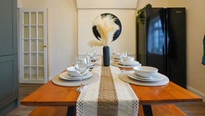 A dining table set with plates, glasses, and a vase with dried flowers, with a black refrigerator and a door in the background.