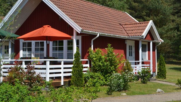 Una casa de madera roja con un porche blanco y un paraguas rojo.