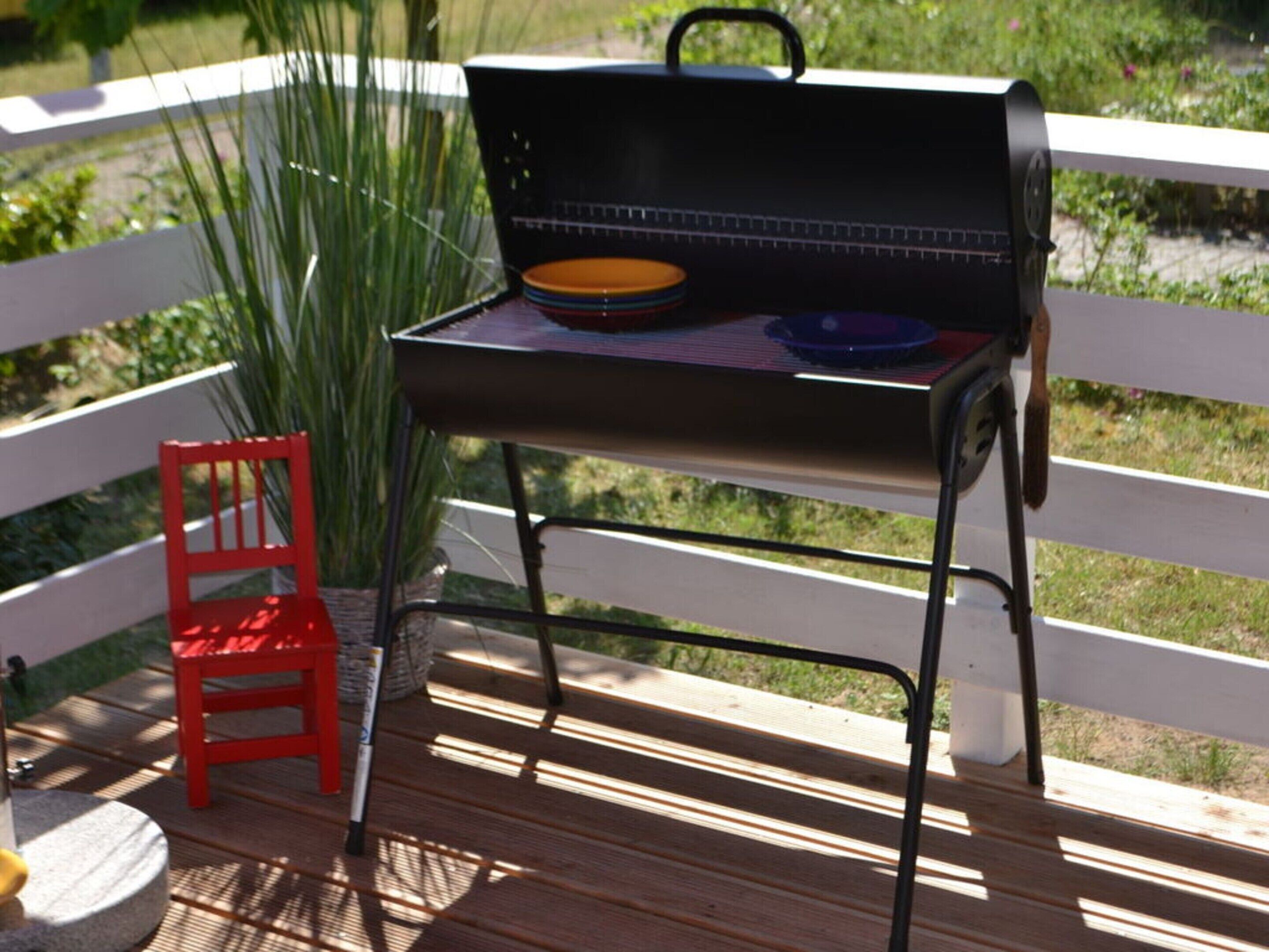 Una parrilla de barbacoa en una terraza de madera con una valla blanca al fondo.