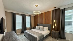 A modern hotel room with a large bed, a wooden nightstand, a desk, and a television. - Last Minute Disney! Private Pool, Hot Tub, Game Room & Themed Bedrooms. Book Now! #110995 (Orlando)