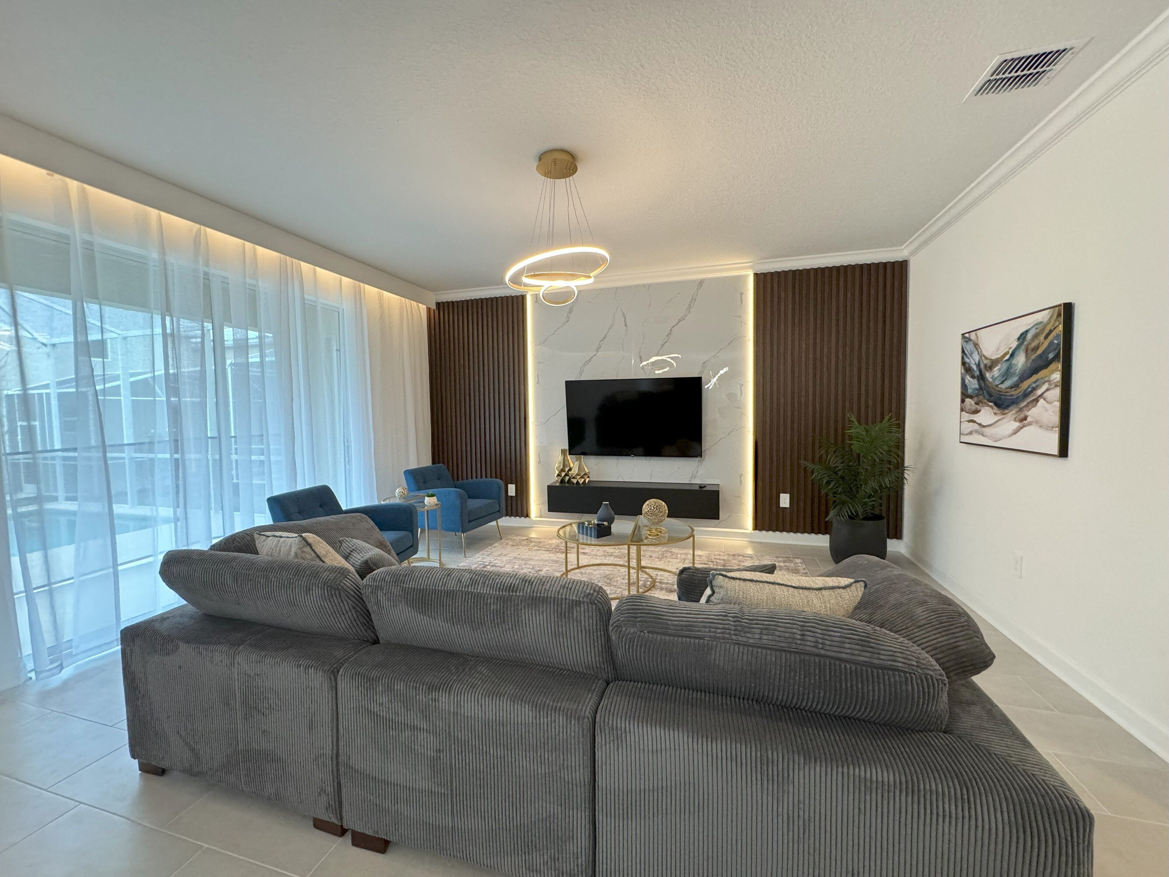 Een moderne woonkamer met een hoekbank, een televisie en een groot raam met transparante gordijnen.