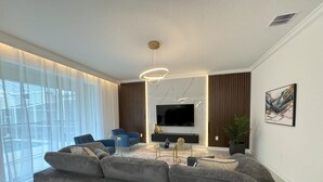 A modern living room with a sectional sofa, a TV, and a large window with sheer curtains. - Last Minute Disney! Private Pool, Hot Tub, Game Room & Themed Bedrooms. Book Now! #110995 (Orlando)