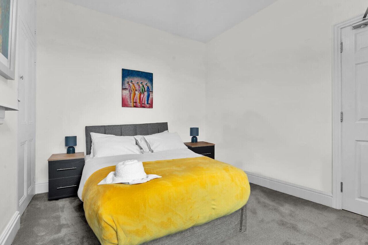 Quarto com cama, mesas de cabeceira, um quadro e uma porta.