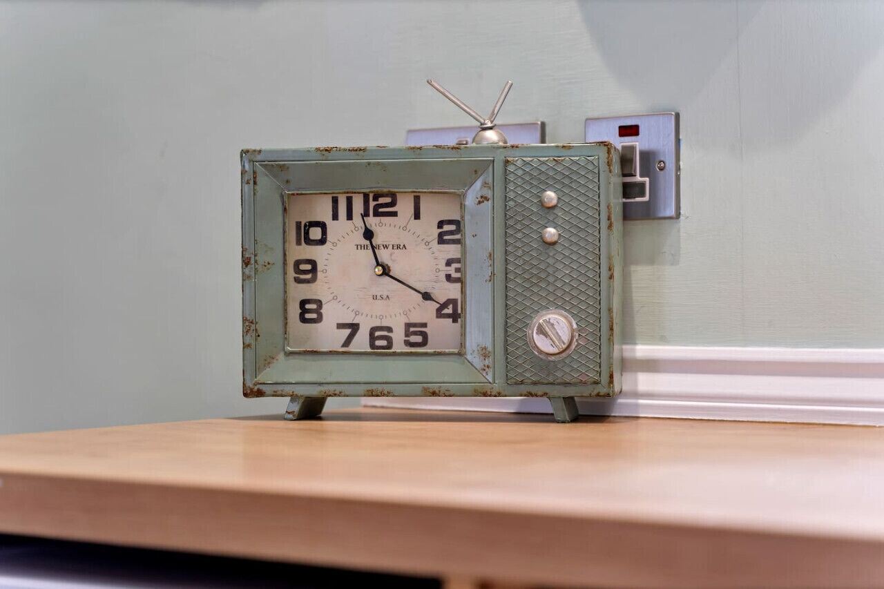 A vintage Thinline Era USA clock with a radio on top, placed on a wooden surface against a light green wall.