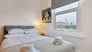 A hotel room with a bed, a window with a view, a painting on the wall, and a towel on the floor.