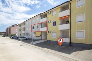 En række boligbygninger med flere etager og altaner, et parkeringsskilt og et fodgængerfelt.
