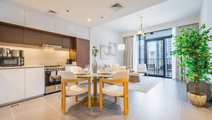 A modern kitchen with white cabinets, stainless steel appliances, and a dining area with a round table and chairs. - Charming 1BR Apartment in Creek Edge Tower 1, Dubai Creek Harbor by Deluxe Holiday Homes (Dubai)