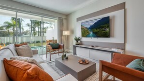 A modern living room with a large flat-screen TV mounted on the wall, a sofa, a coffee table, and a chair. - Last Minute Disney Getaway! Private Pool & Themed Bedrooms. Book Now! #104045 (Orlando)