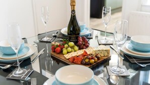 Una mesa dispuesta para una comida, con una botella de champán Nozeco, varios tipos de queso, uvas y aceitunas.