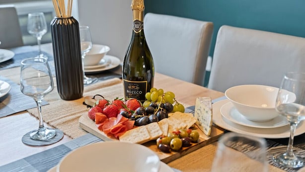 A table set for a meal with a bottle of Nozeco wine, a variety of cheeses, strawberries, grapes, and crackers.
