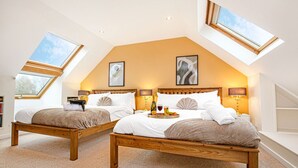 A bedroom with two wooden beds, a skylight, and a small dining table with a tray of food and drinks.