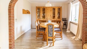 A dining area with a brick archway, wooden dining table, chairs, and a cabinet with glass doors. - Holiday Home Tidenkieker (Nordstrand)