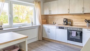 A modern kitchen with white cabinets, a wooden countertop, and a window with curtains. - Holiday Home Tidenkieker (Nordstrand)