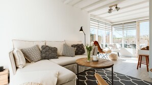 A modern living room with a sectional sofa, a round coffee table, and a view of the outdoors. - Holiday Home in Hygge Style (Ouddorp)