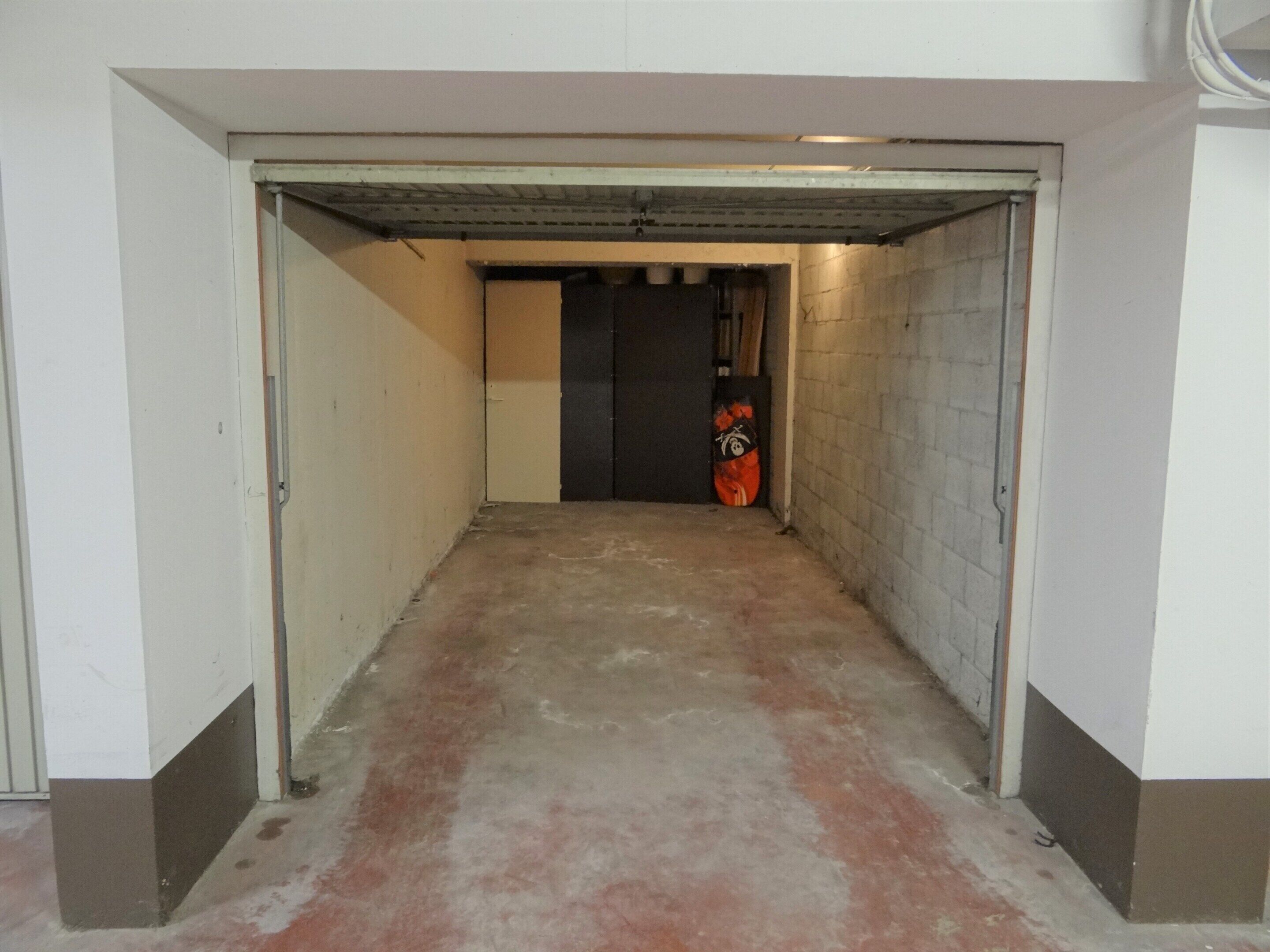 Un estrecho pasillo con piso de concreto y techo metálico, que conduce a una puerta oscura al final.