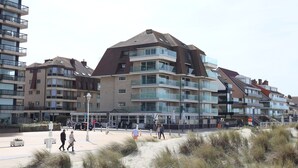 A coastal residential building with multiple balconies, a sandy foreground, and a clear sky. - Apartment in Nieuwpoort by Sandy Beaches (Nieuwpoort)