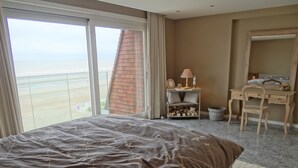 A hotel room with a large bed, a desk, a chair, and a view of the beach. - Apartment in Nieuwpoort by Sandy Beaches (Nieuwpoort)