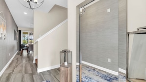 A modern hallway with a staircase, a dining area in the background, and a door with a textured panel. - Last Minute Disney Getaway! Private Pool & Themed Bedrooms. Book Now! #112813 (Orlando)