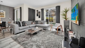 A modern living room with a grey sectional sofa, a coffee table, and a large TV on the wall. - Last Minute Disney Getaway! Private Pool & Themed Bedrooms. Book Now! #112813 (Orlando)