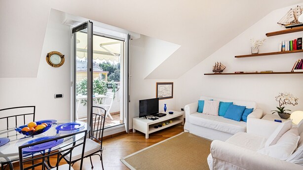 A modern living room with a glass dining table, white sofa, and a TV on a white stand.