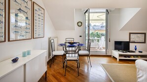 A modern, well-lit room with a dining area, a TV, and a balcony with a view.
